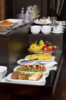 Un bufé con diversas opciones de comida, incluyendo frutas, verduras y pastelería.