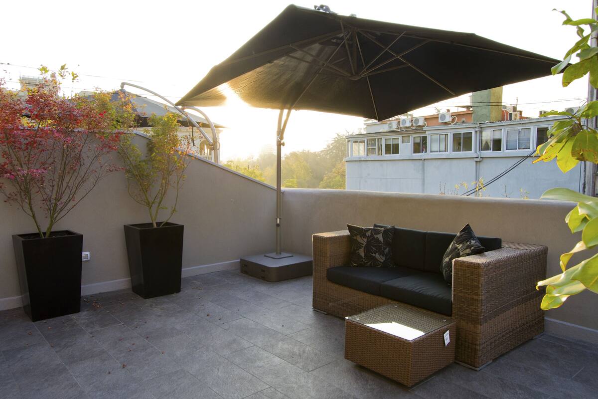 A balcony with a sofa, a table, and an umbrella.
