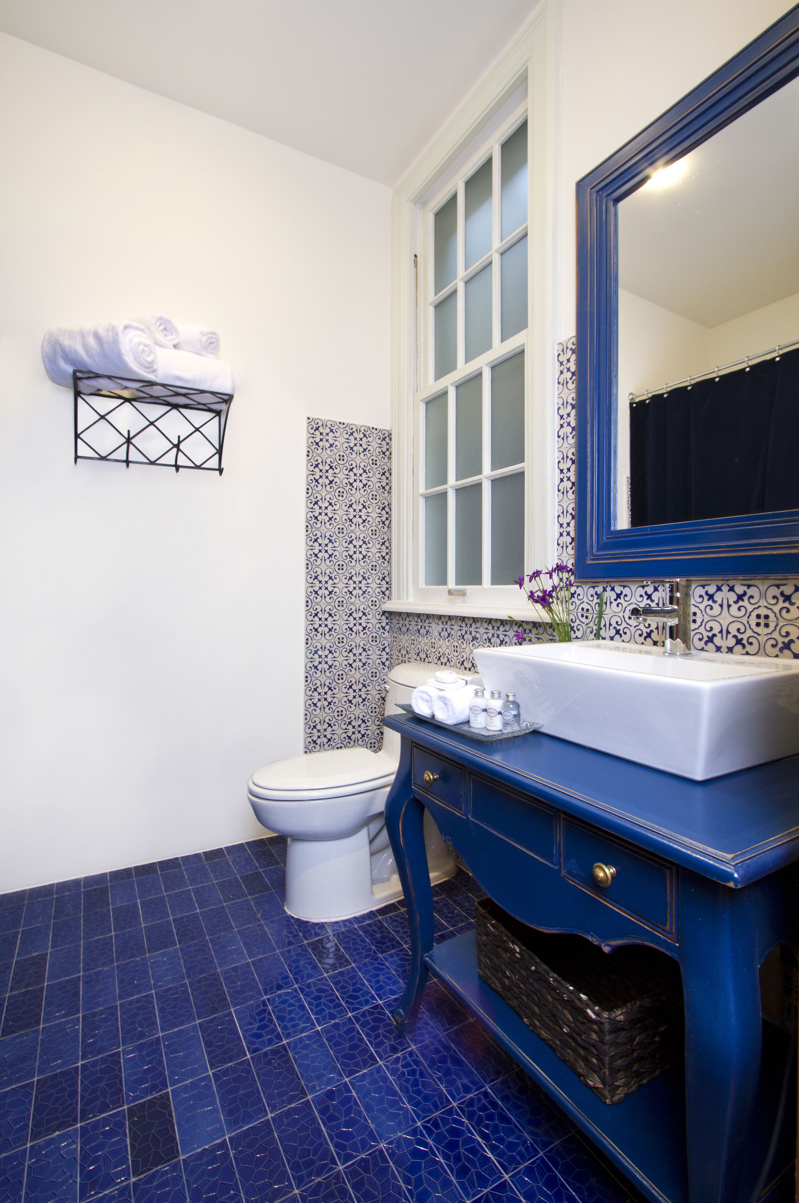 A bathroom with a white toilet, a blue vanity with a mirror, and a blue tiled floor.
