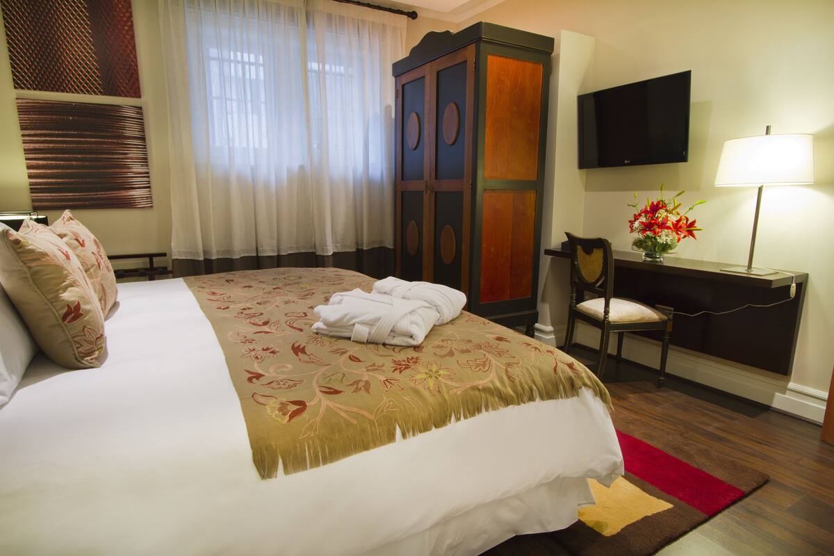 A hotel room with a large bed, a desk with a chair, a TV, and a lamp.