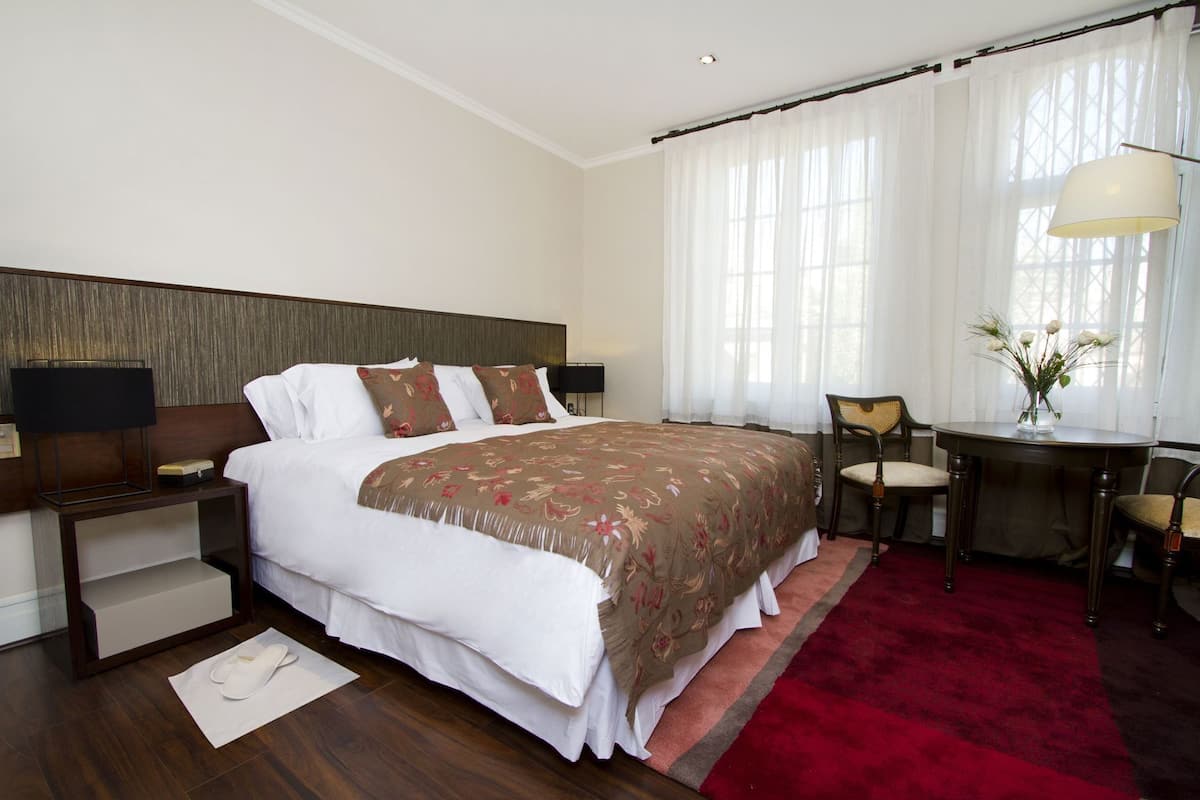 A hotel room with a large bed, a desk with a chair, a lamp, and a vase with flowers.