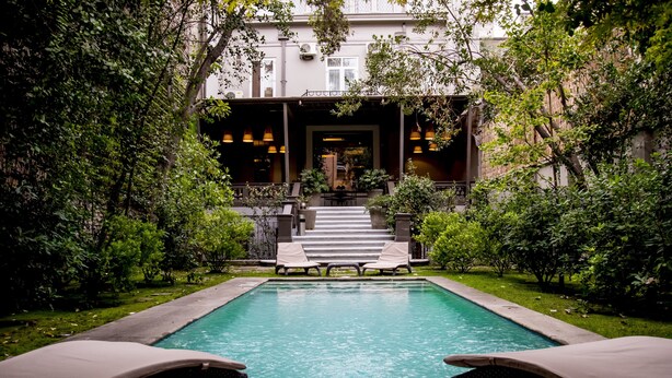 A rectangular pool with lounge chairs on either side, surrounded by greenery and a building with a staircase leading to an entrance. - Casa Bueras Boutique Hotel (Santiago)
