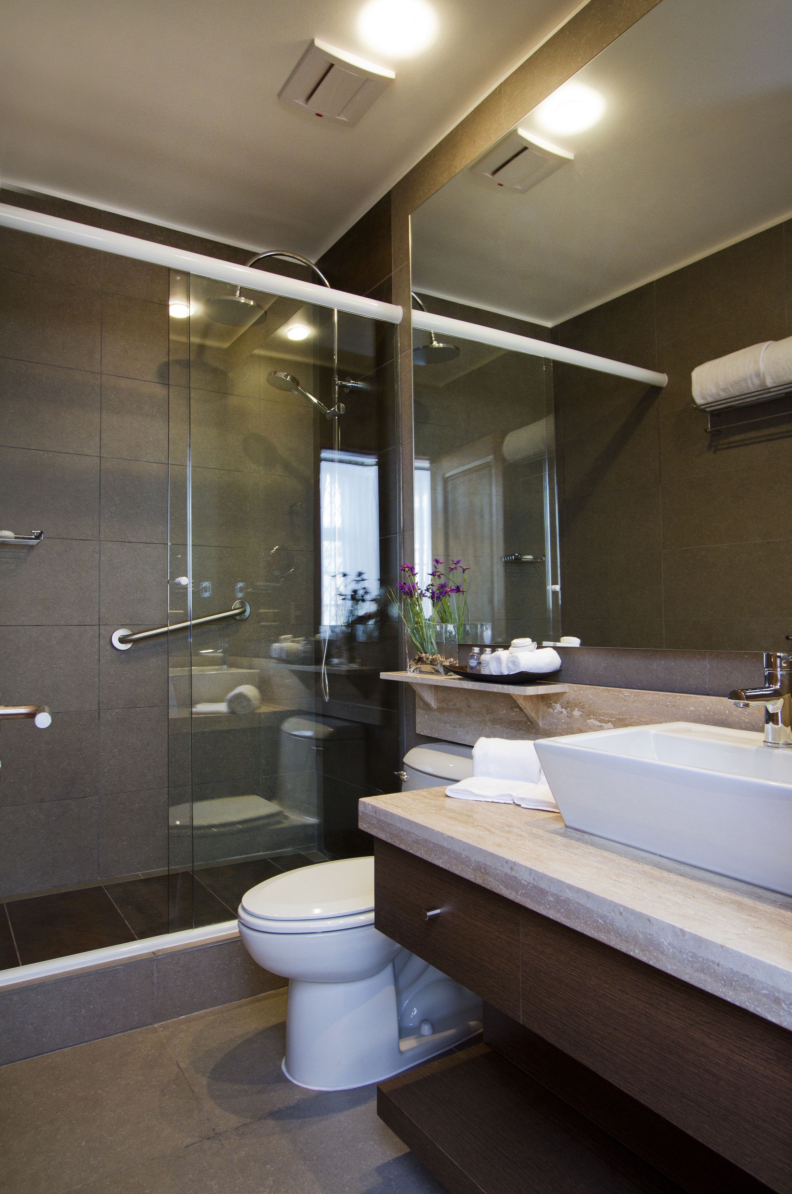 A modern bathroom with a glass-enclosed shower, a white toilet, a large mirror, and a bathtub.