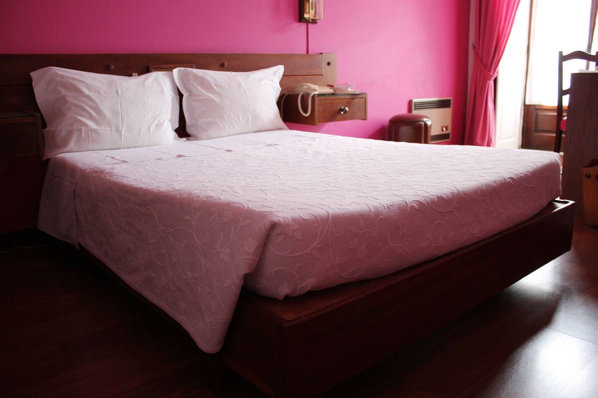 A large bed with a wooden headboard, a bedside table with a lamp, and a nightstand with a telephone.