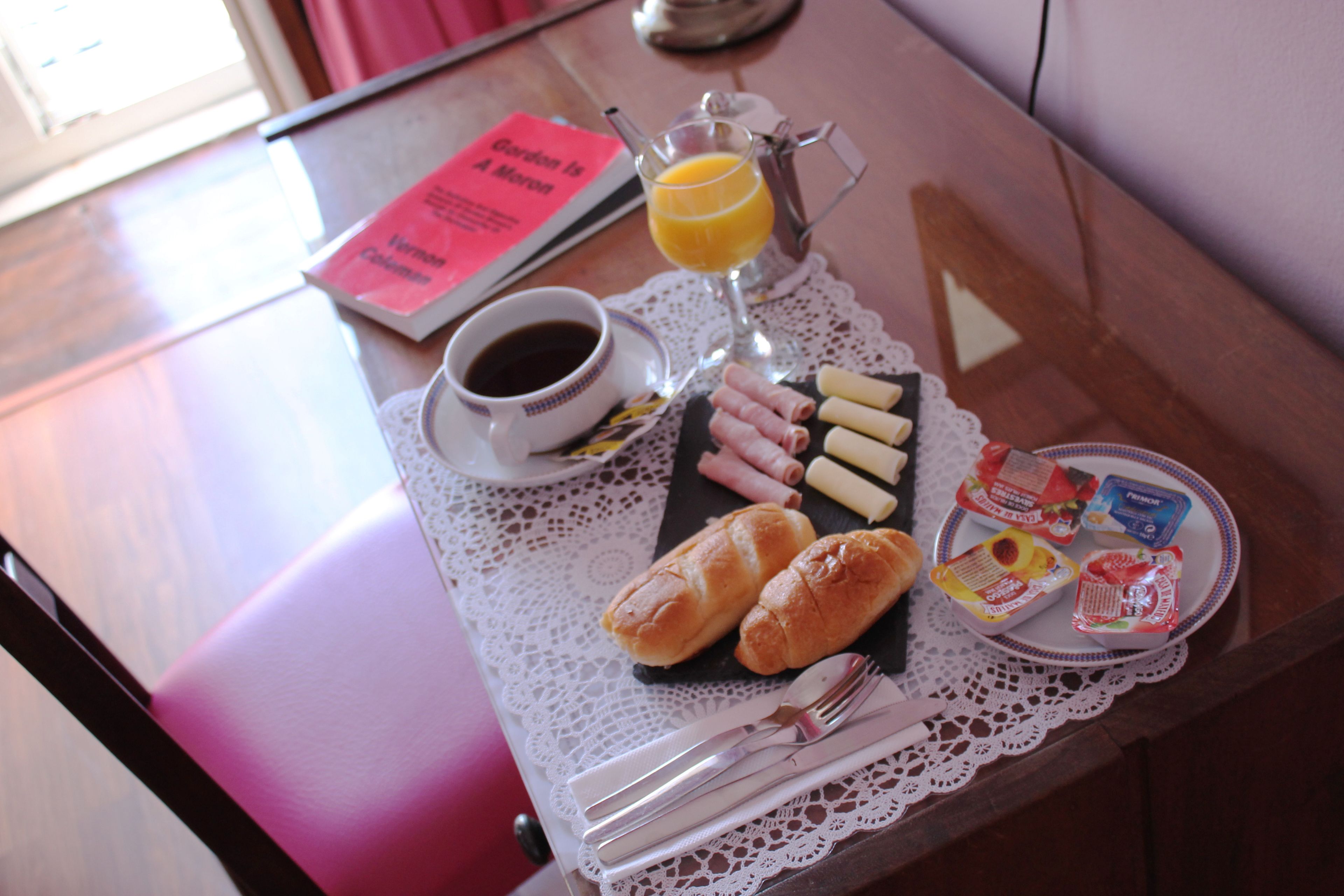 A breakfast tray with croissants, ham, and a glass of orange juice on a wooden table.
