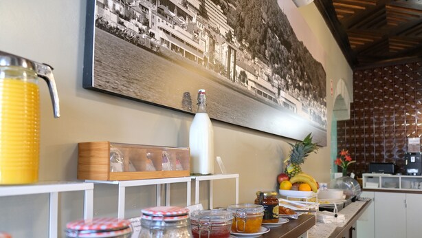 Una barra de desayuno con diversas opciones de comida y condimentos, un dispensador grande de jugo y un cuadro en la pared.