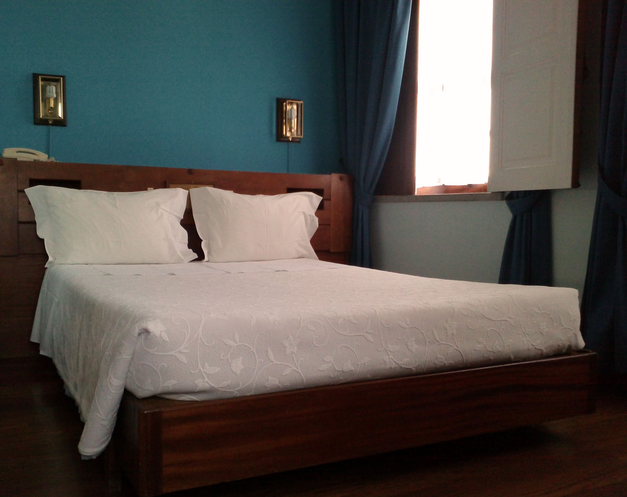 Llits amb llençols blancs i un ambossada de fusta en una habitació amb parets blaves.