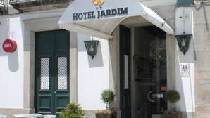 Entrada de un hotel con un letrero que dice "HOTEL JARDIM", asientos al aire libre y plantas en macetas.