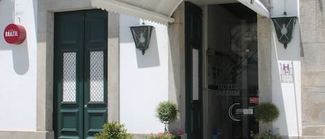 A hotel entrance with a sign reading "HOTEL JARDIM," outdoor seating, and potted plants.