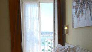 Habitación de hotel con una cama grande, vista al mar a través de una ventana abierta y un cuadro en la pared.
