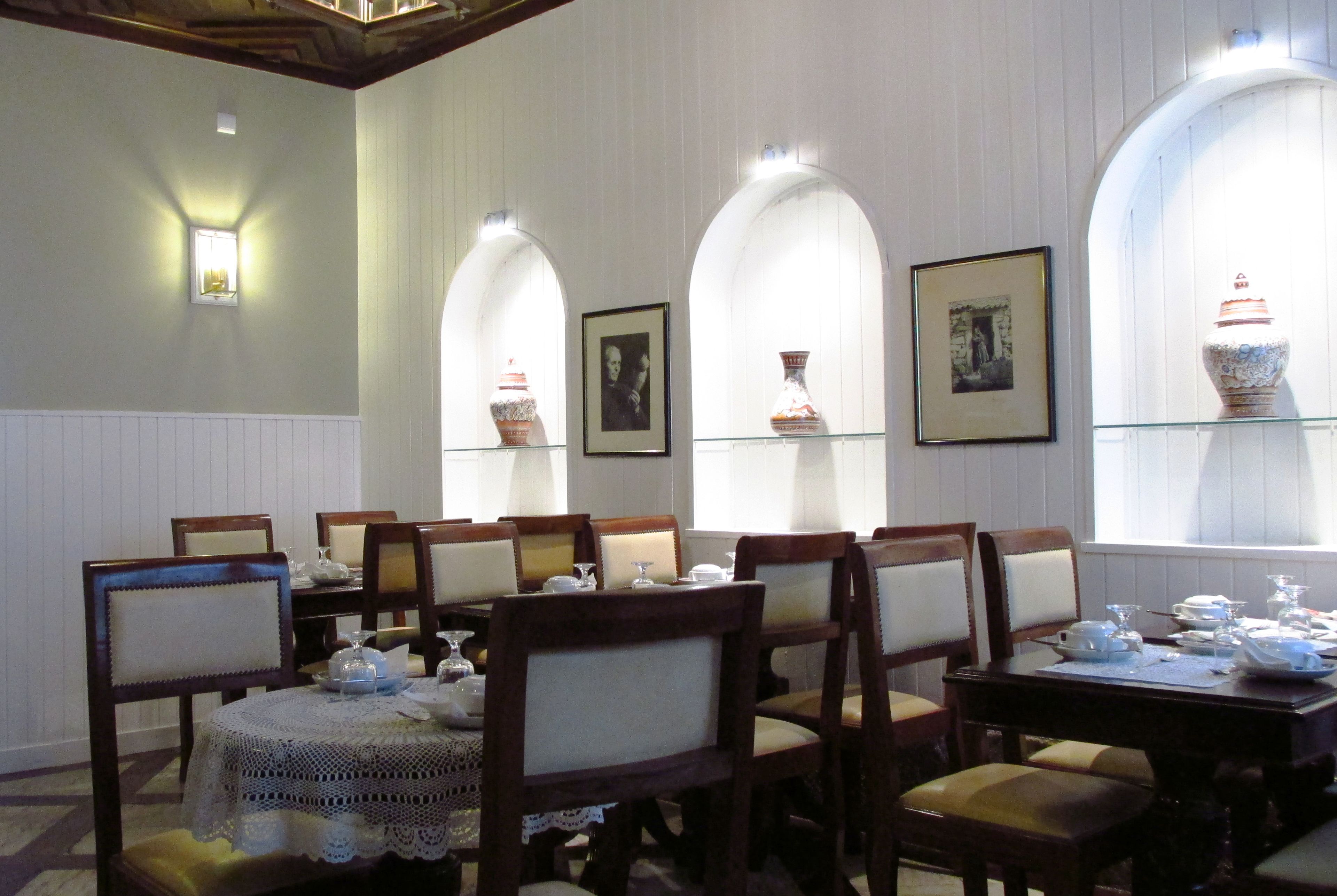 A dining area with wooden chairs and tables, white walls, and arched windows with decorative vases.