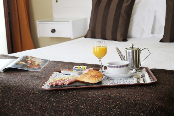Bandeja de desayuno con cruasanes, jamón y un vaso de jugo de naranja sobre una cama en una habitación de hotel.