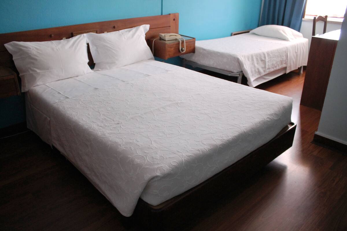 A double bed with a wooden headboard, a bedside table with a lamp, and a small wooden nightstand with a telephone.