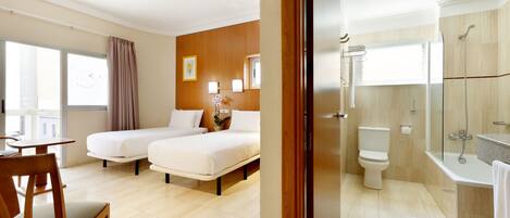 Habitación de hotel con dos camas, baño con ducha y vista a la ciudad.