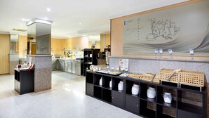 Een hotel lobby met een receptiebalie, een groot muurschilderij en een buffetruimte met diverse soorten eten en verpakkingen.