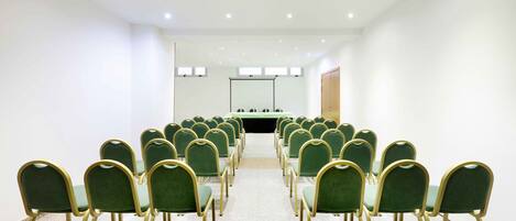 Un salón de conferencias con filas de sillas verdes y una larga mesa en el centro.