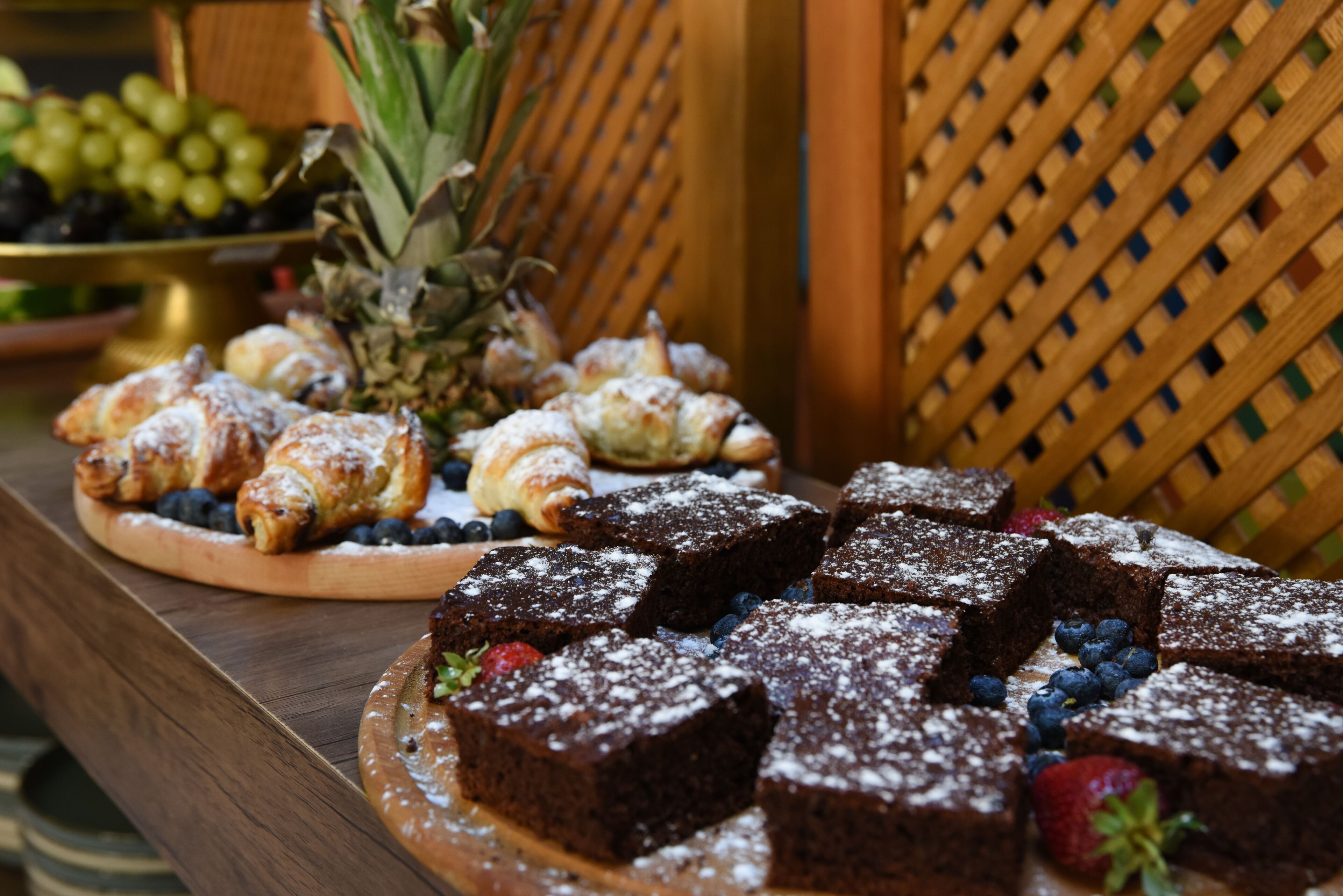 Una mesa de madera con diversos postres, como brownies, pasteles y frutas frescas.