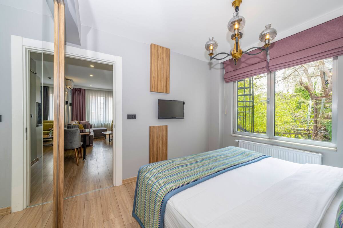 Un dormitorio con una cama, un televisor, un ventanal con vistas a zonas verdes y suelo de madera.