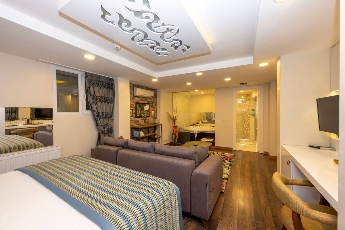 Habitación de hotel moderna con sofá cama, escritorio, baño con ducha de vidrio y zona de comedor.