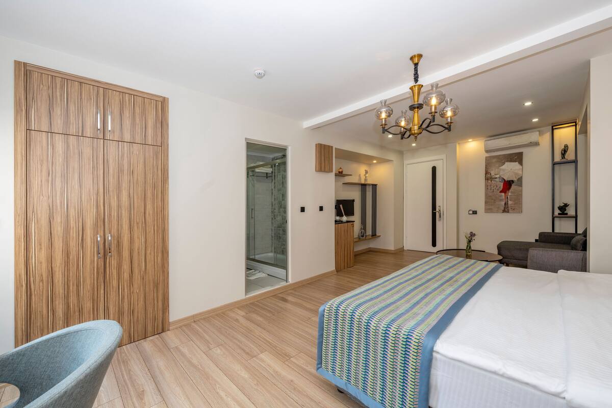 Una habitación de hotel moderna con una cama grande, un armario de madera, una zona de estar y un baño con ducha de vidrio.