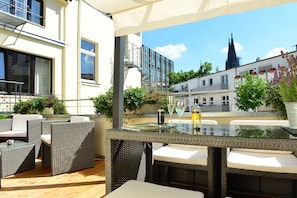 An outdoor patio with wicker furniture, a glass-top table, and potted plants. - Hotel Domspitzen (Cologne)
