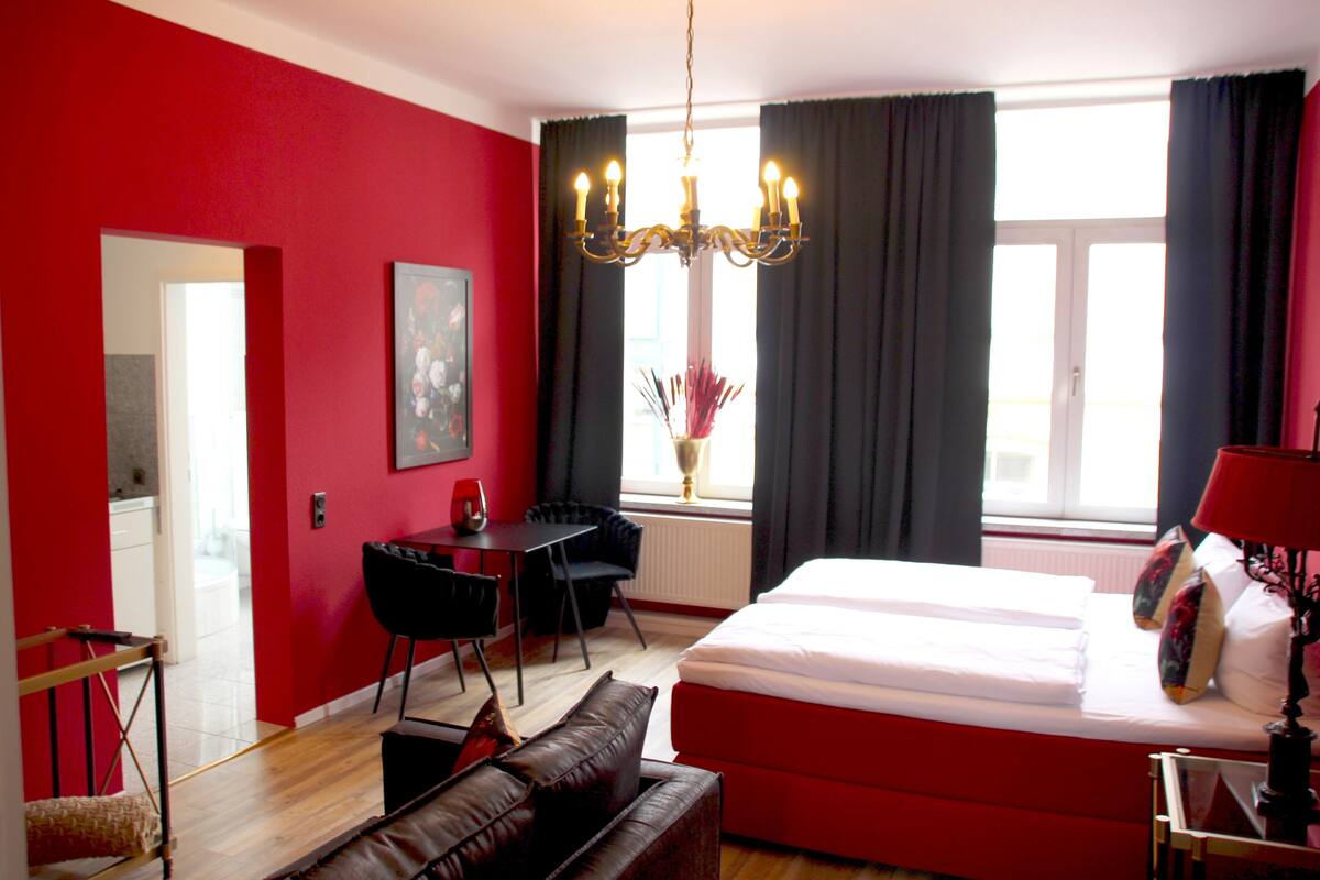 Une chambre d’hôtel avec un mur rouge, un grand lit, un bureau et un lustre.