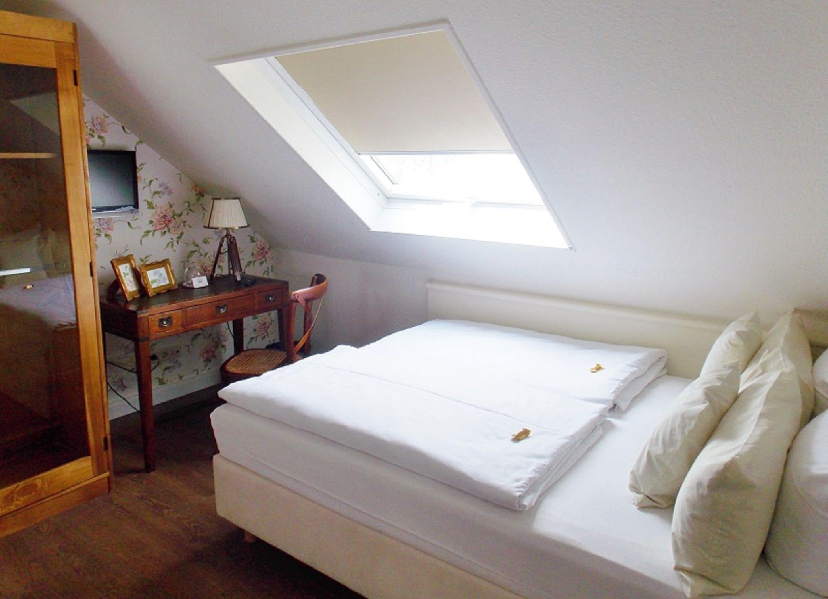 A bedroom with a skylight, a bed, a desk with a lamp, and a chair.