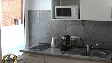 Une cuisine avec des meubles blancs, un four à micro-ondes, une bouilloire, une machine à café et un évier.