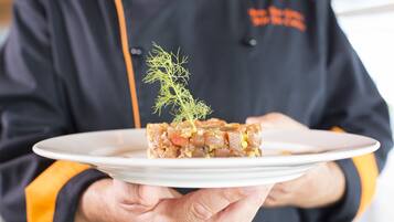 A person holding a white plate with a food dish garnished with a sprig of dill.