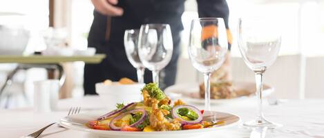 A dining table with a plate of food, wine glasses, and cutlery.