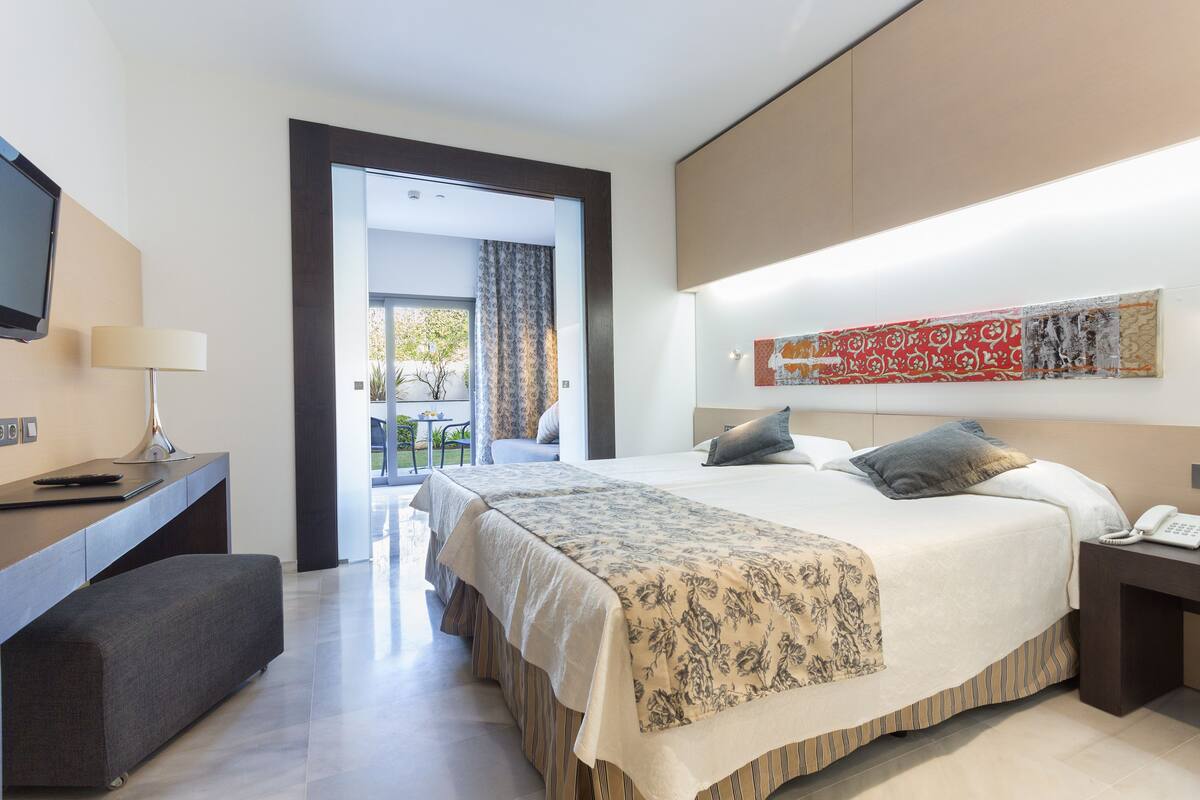 A hotel room with a bed, bedside table, lamp, and a TV on a desk.
