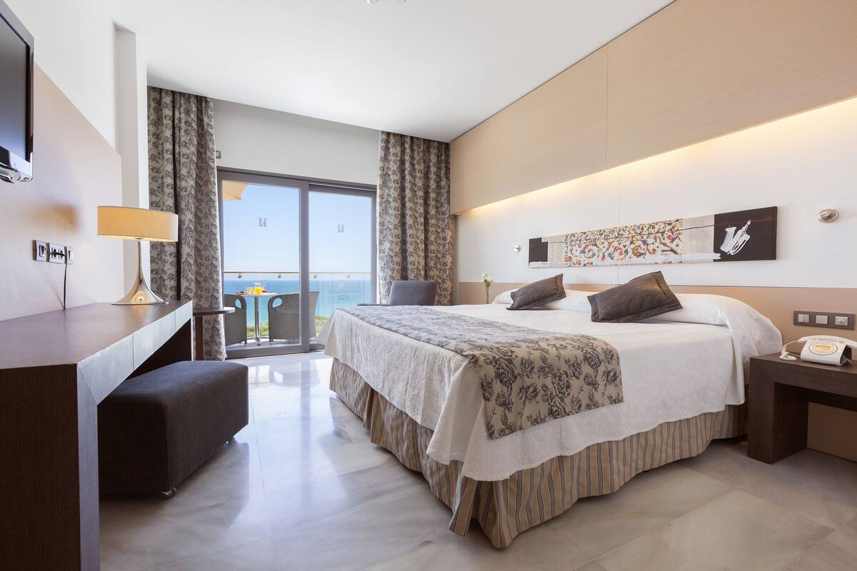 A modern hotel room with a large bed, a desk, and a balcony with a view.