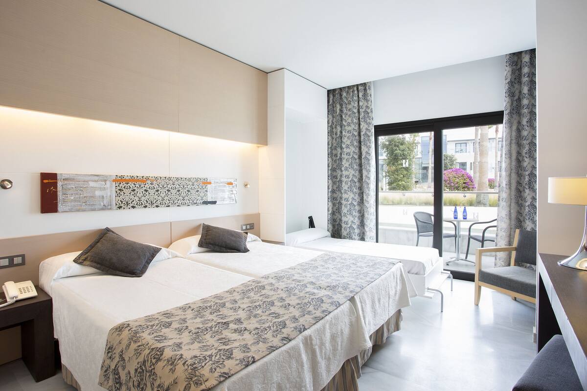 A hotel room with two beds, a desk, and a view of the outside.