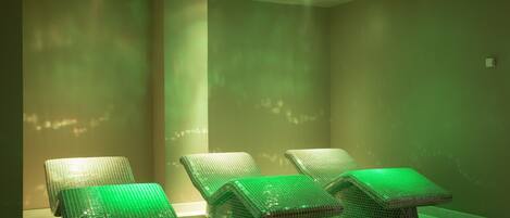 Une pièce où se trouvent quatre fauteuils de massage recouverts de carreaux verts, disposés en rangée contre un mur sobre.