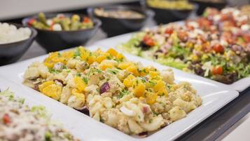 A buffet with various dishes including a potato salad with orange chunks, a salad with mixed greens and tomatoes, and other assorted dishes.