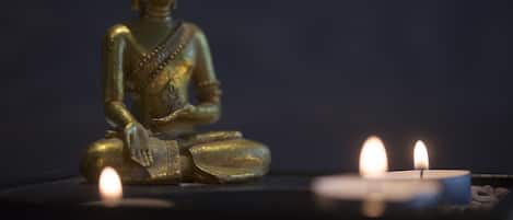 A golden Buddha statue seated with a candle in front.