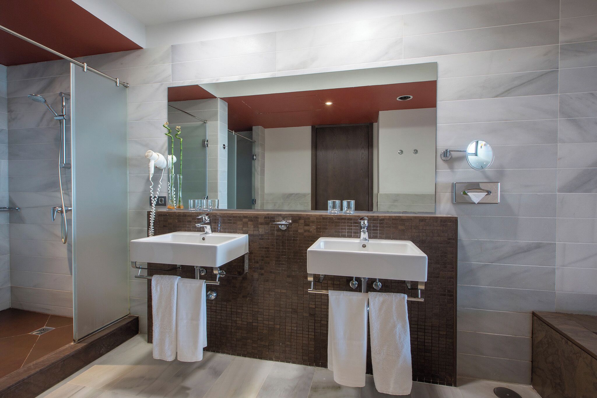 A modern bathroom with two sinks, a glass shower enclosure, and a large mirror above the sinks.