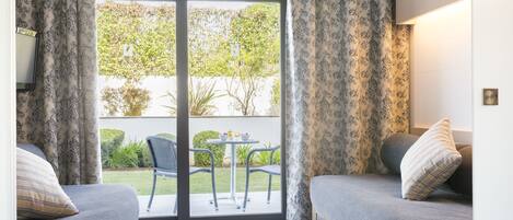 A room with two beds, a sliding glass door to a patio with a table and chairs, and a view of greenery outside.