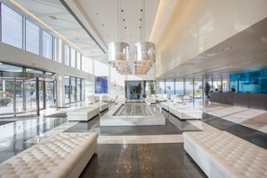 Un vestíbulo espacioso con una zona de estar central, ventanas amplias y candelabros modernos.