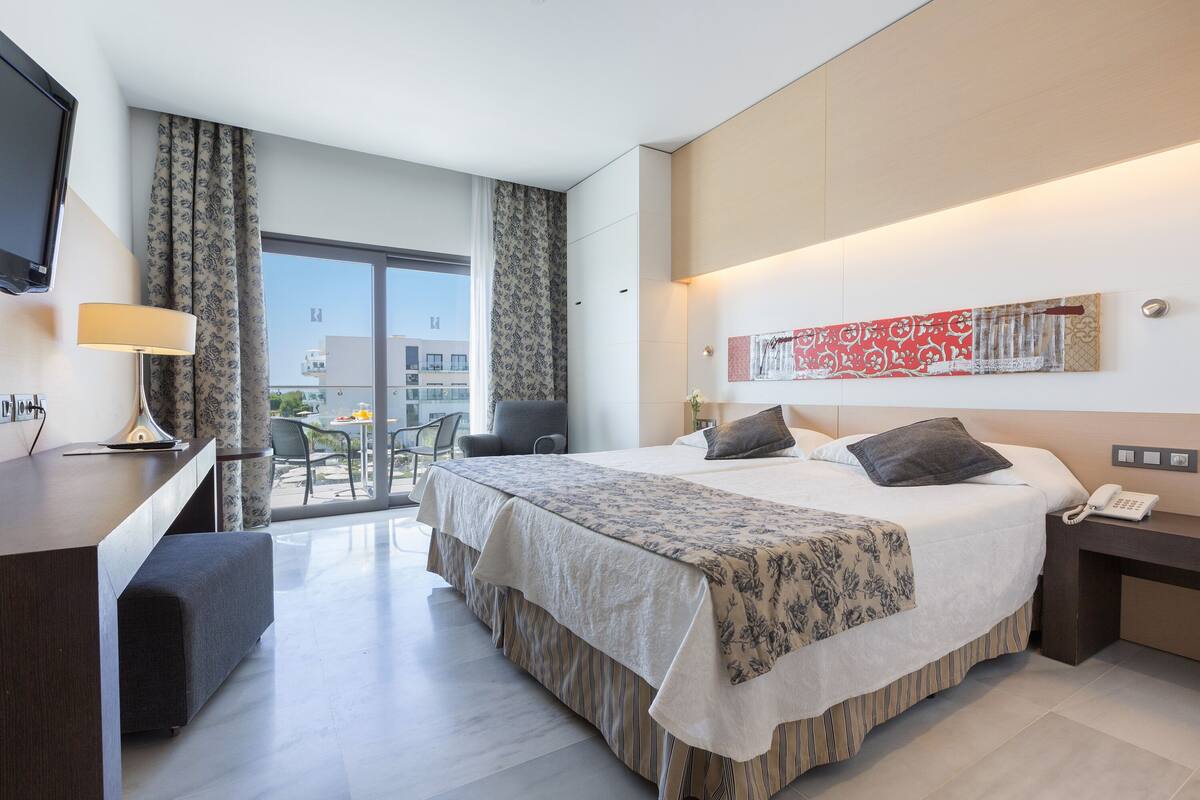 A modern hotel room with a large bed, a desk, a chair, and a view of the city.