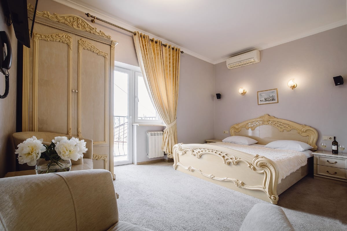 A bedroom with a large bed, a wardrobe, a bedside table with a bottle and glasses, and a window with curtains.