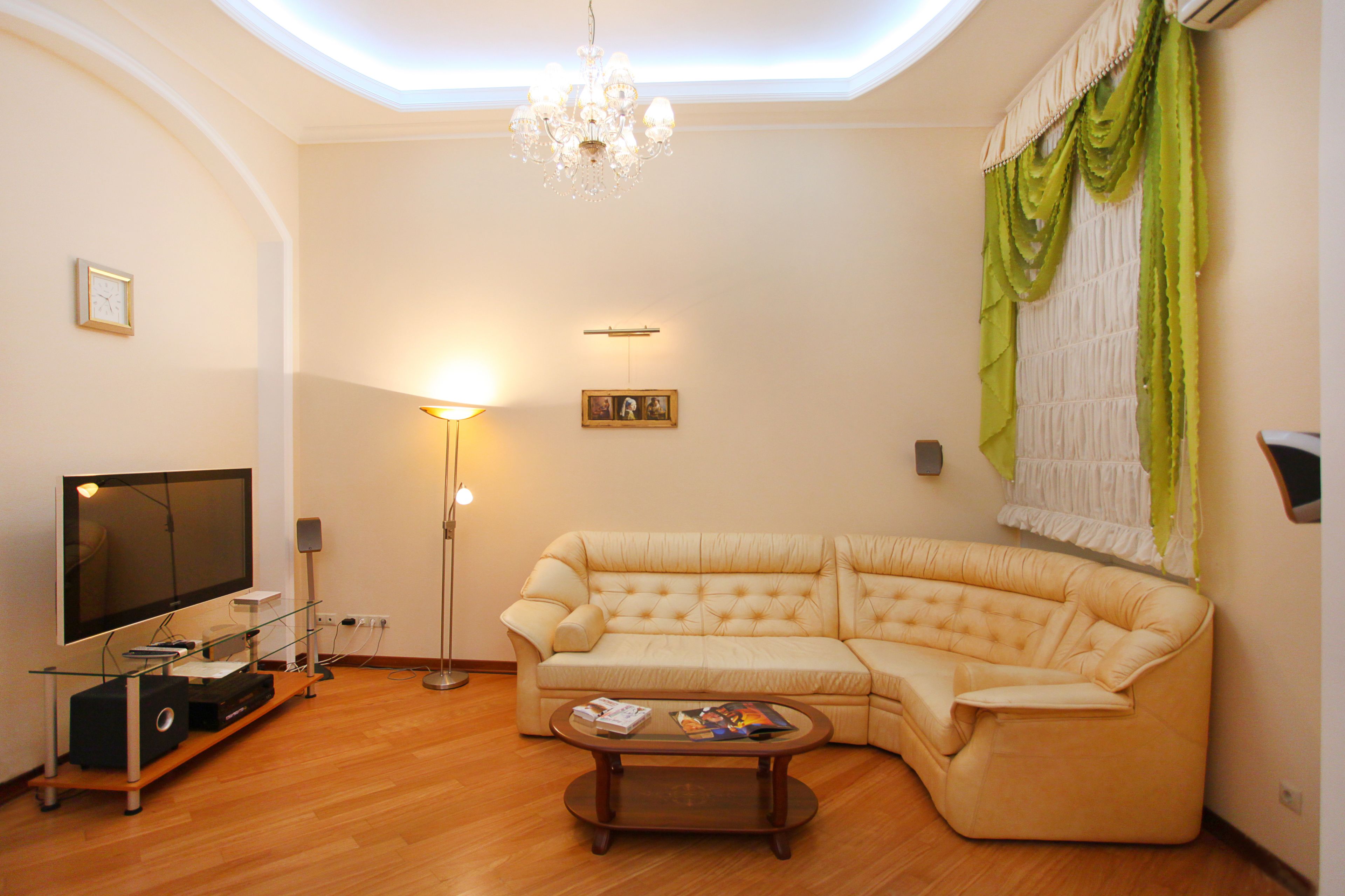 A living room with a large L-shaped sofa, a flat-screen TV, a coffee table, and a chandelier.