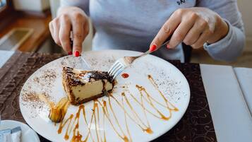 A person cutting a slice of cheesecake with caramel sauce on a white plate.