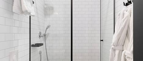 Un baño moderno con ducha de vidrio, paredes con azulejos blancos, inodoro blanco y un perchero para toallas.