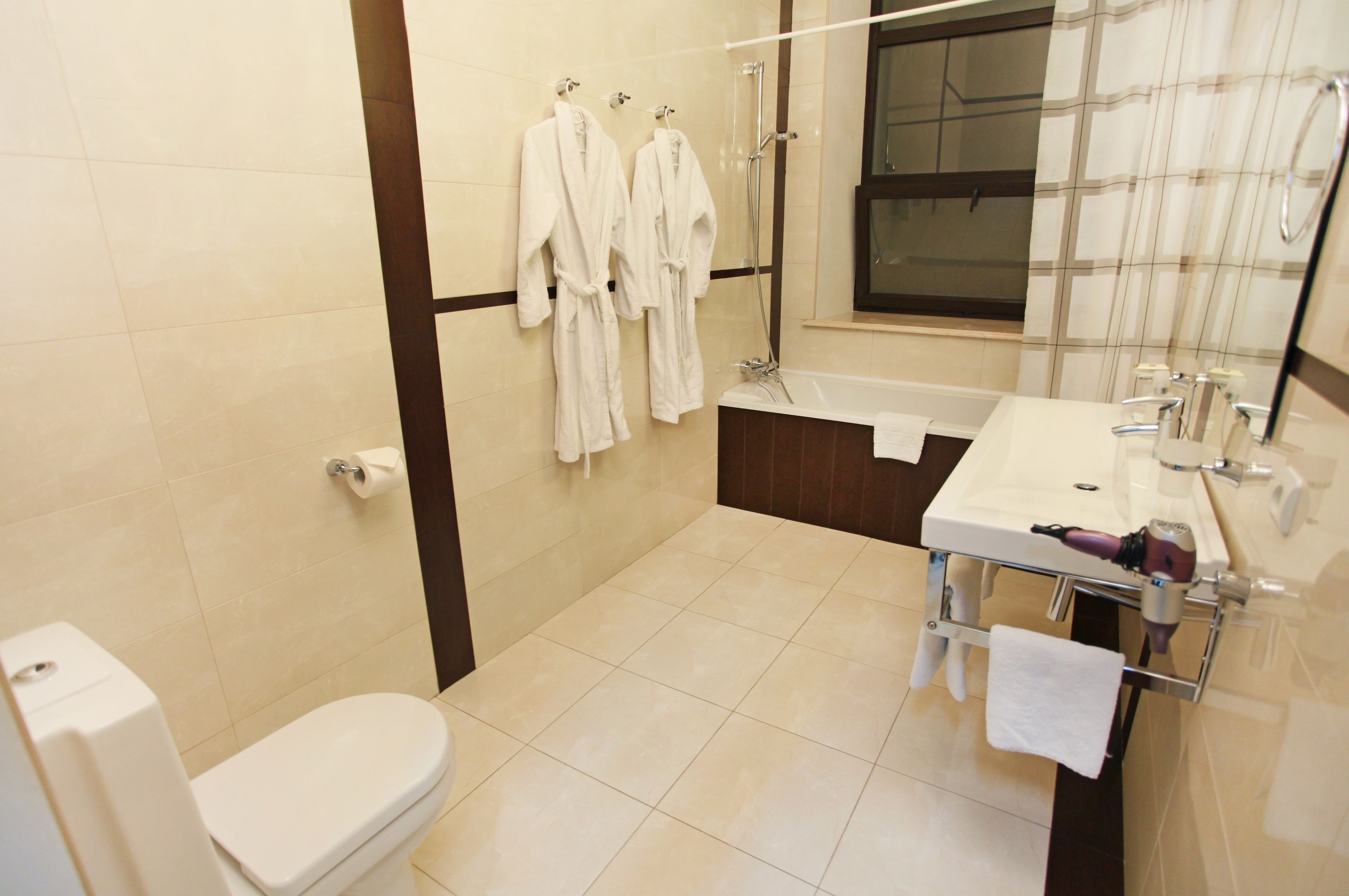 Un baño con inodoro, lavamanos, ducha y dos albornoces blancos colgados en la pared.