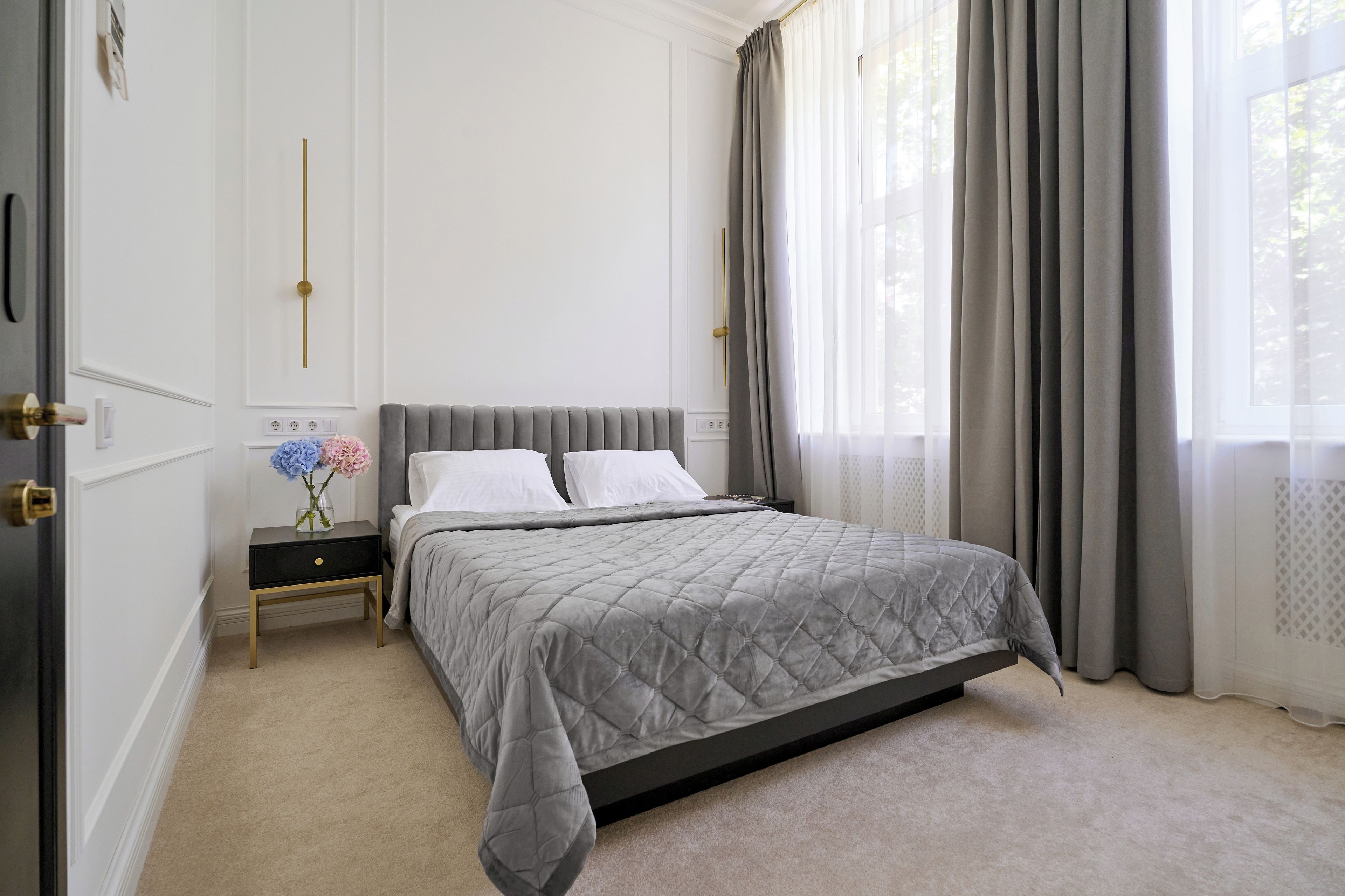 A bedroom with a bed, bedside table, and a nightstand with flowers.
