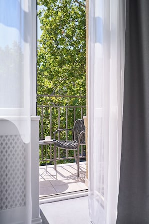 An open balcony with a table and chairs, a view of trees, and a white railing.