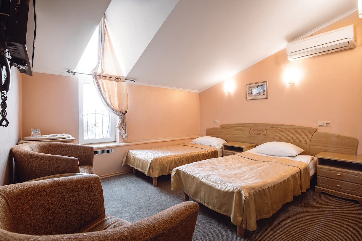 A hotel room with two beds, a desk, a chair, and a window with curtains.