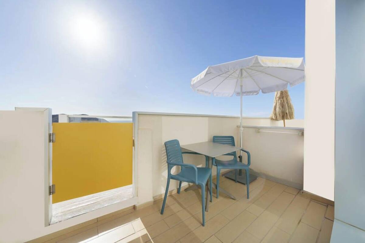 A balcony with a table and chairs, a white umbrella, and a yellow partition.