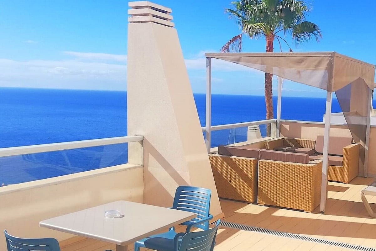 A deck with a table and chairs, a covered seating area, and a view of the ocean.